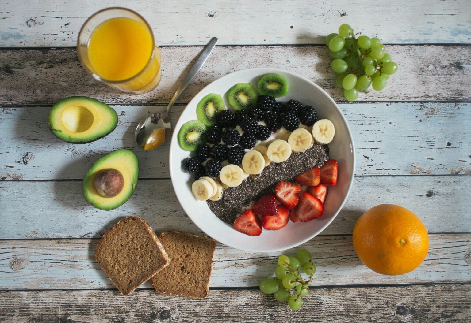 Fruit salad with banana, strawberries, kiwi, blackberries. Additionally avocado, orange, grapes and fresh orange juice served with slices of bread.